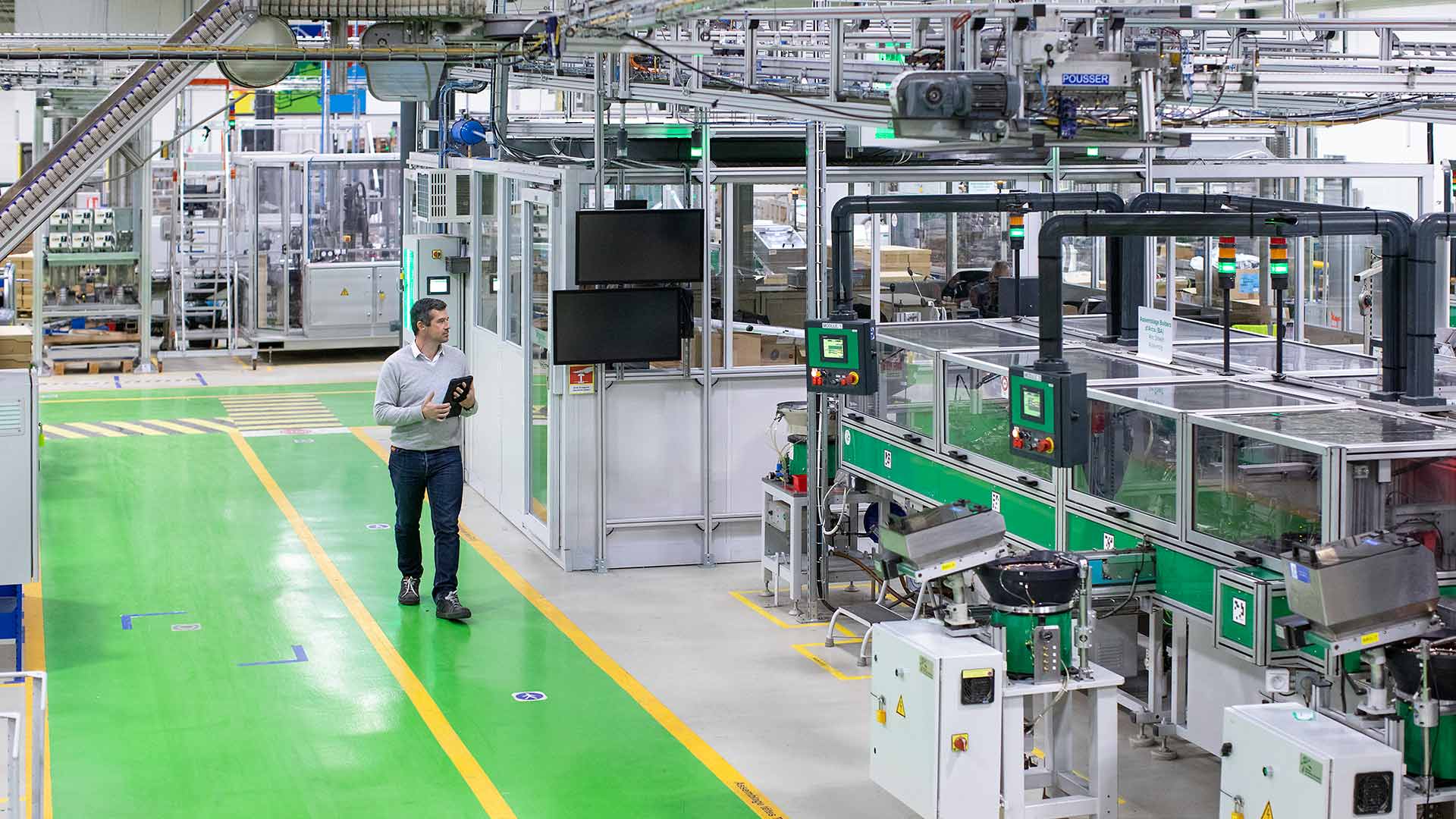 A man walking inside a smart factory while holding a digital tablet in hand.